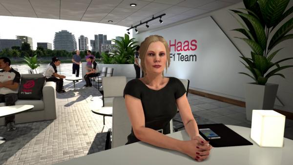 Screenshot: Eine blonde Formel 1 Managerin sitzt in einer Lobby an einem Tisch