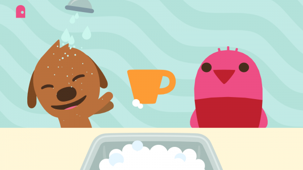 Screenshot: eine braune Hundefigur und eine rosa Vogelfigur stehen vor einem Waschbecken. Zwischen ihnen ist eine orange Tasse. Die Hundefigur wird von einer Brause mit Wasser bespritzt und lacht dabei.